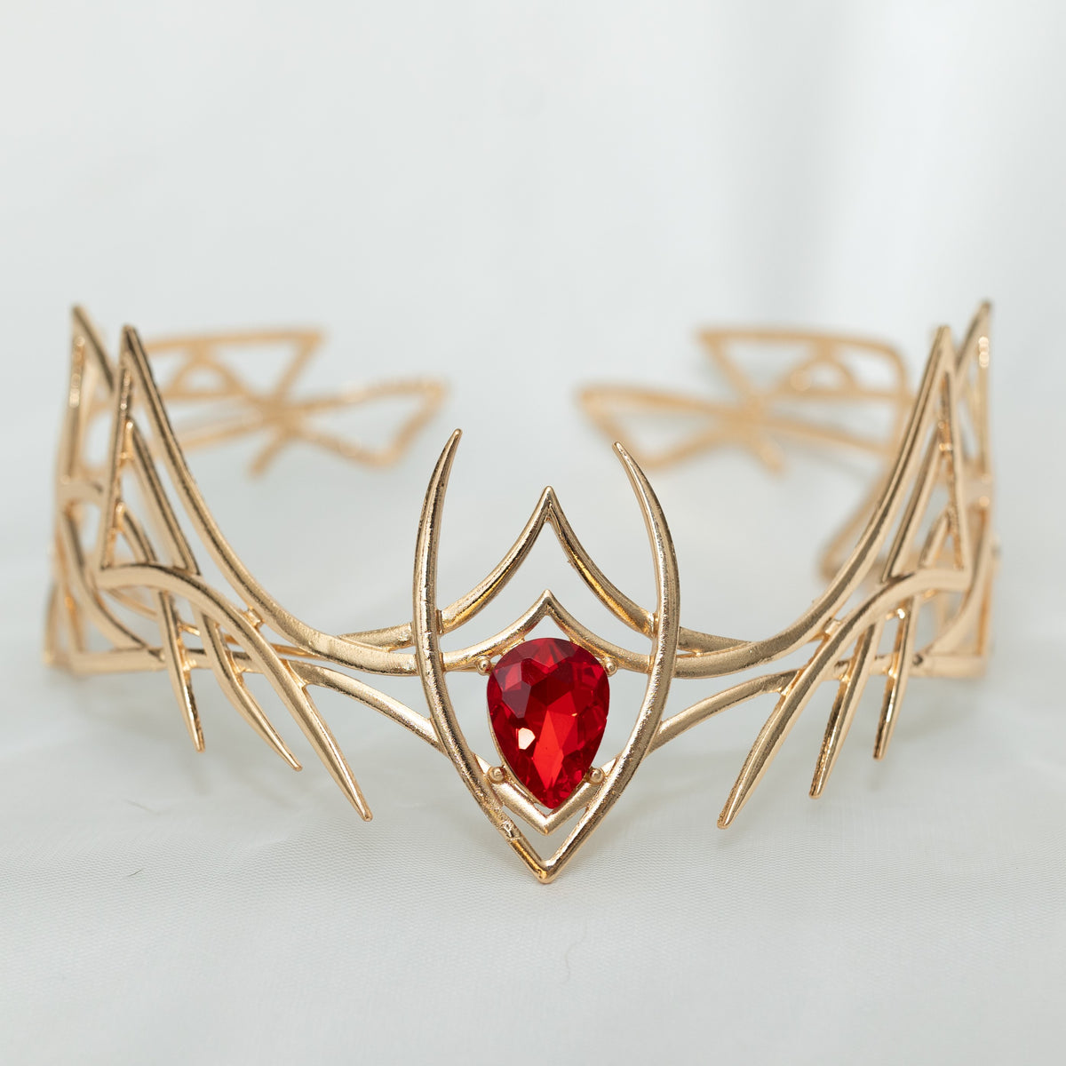Gold tiara with a red gemstone on a light gray background