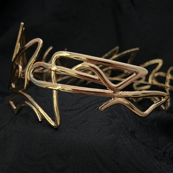A gold abstract wire art piece with organic, flowing lines, displayed against a textured black fabric background.