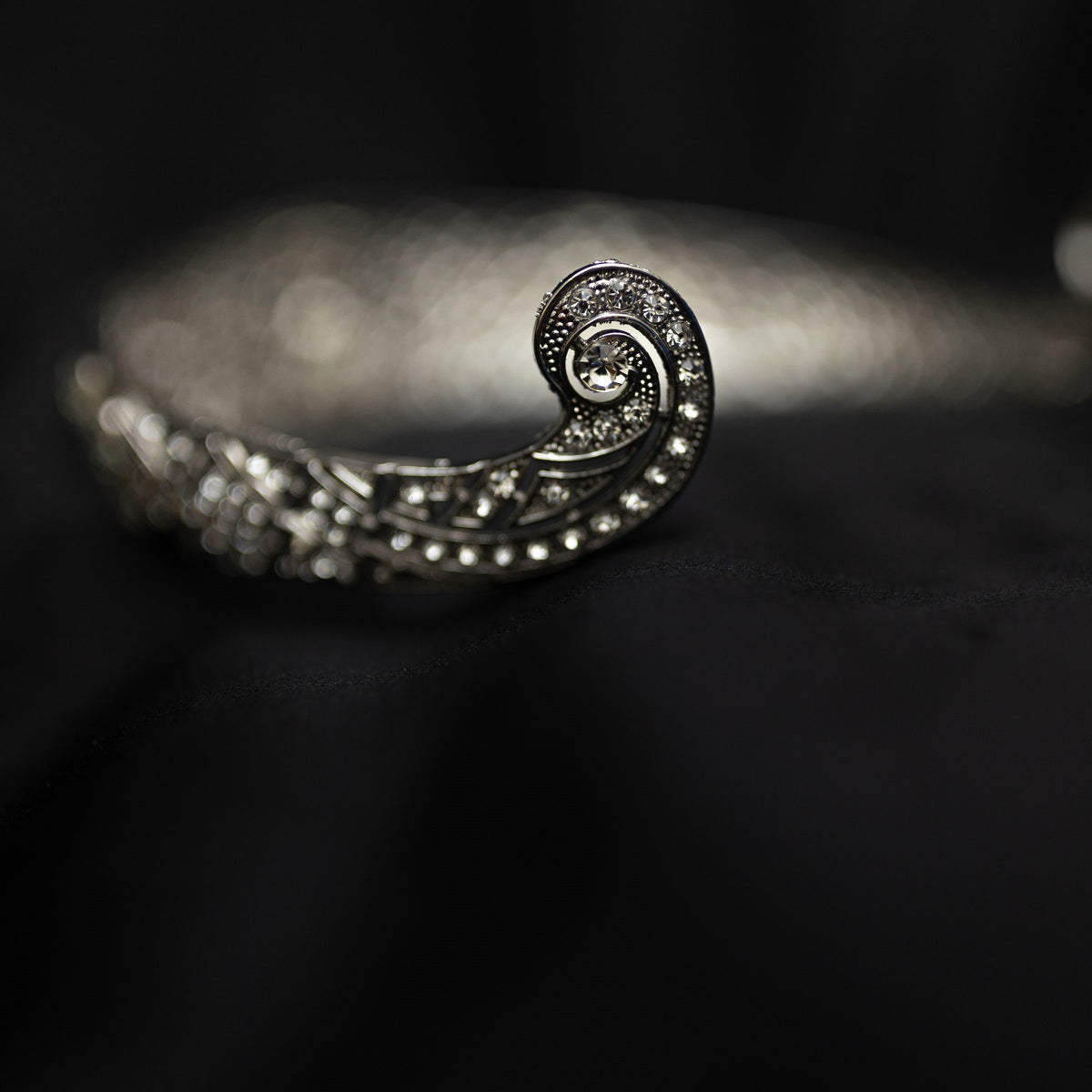 A silver-colored metal tiara with clear crystals set around the circumference, featuring a central decorative front - End View 