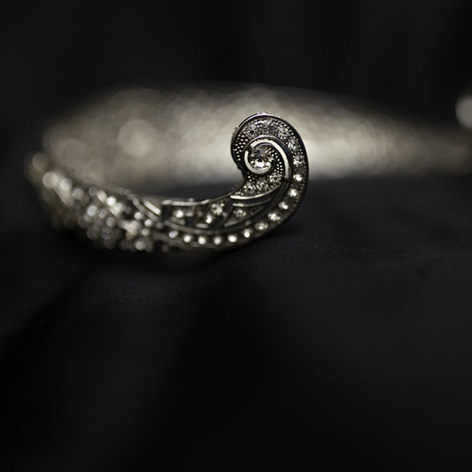 A silver-colored metal tiara with clear crystals set around the circumference, featuring a central decorative front - End View 