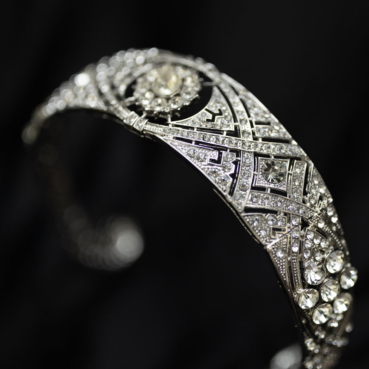 A silver-colored metal tiara with clear crystals set around the circumference, featuring a central decorative front - Side Front View 