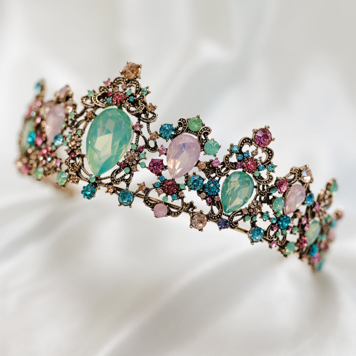 Tiara with multi color tear drop stones, light blue, light ping, teal, with small round stones throughout set in antique gold color metal - Angled Front View 
