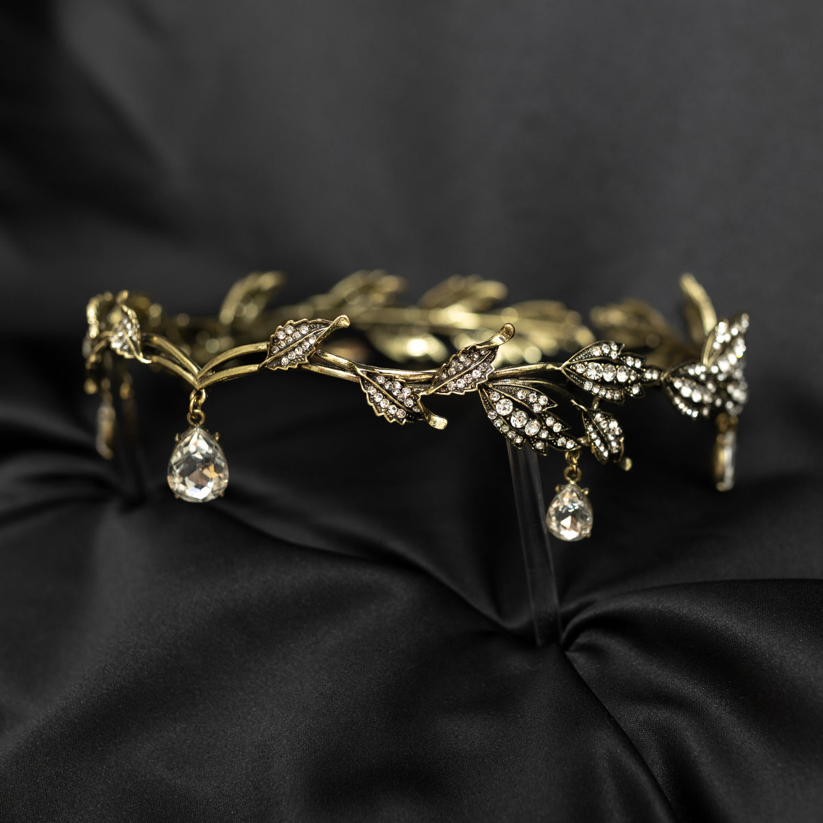 An antique gold circlet crown with leaf details and a crystal drop at the center, displayed on a black background.