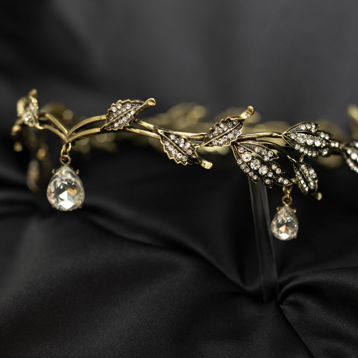An antique gold circlet crown with leaf details and a crystal drop at the center, displayed on a black background.