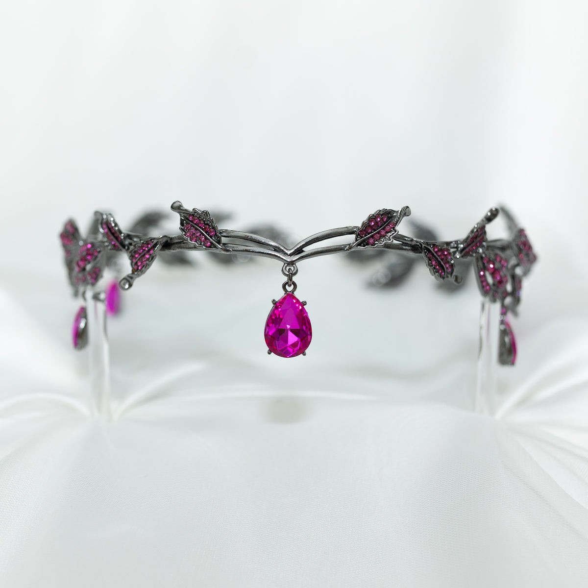 An elegant circlet featuring a hot pink crystal drop as the centerpiece, antique silver color metal with leaf-shaped embellishments and smaller pink crystals, set against a white background.