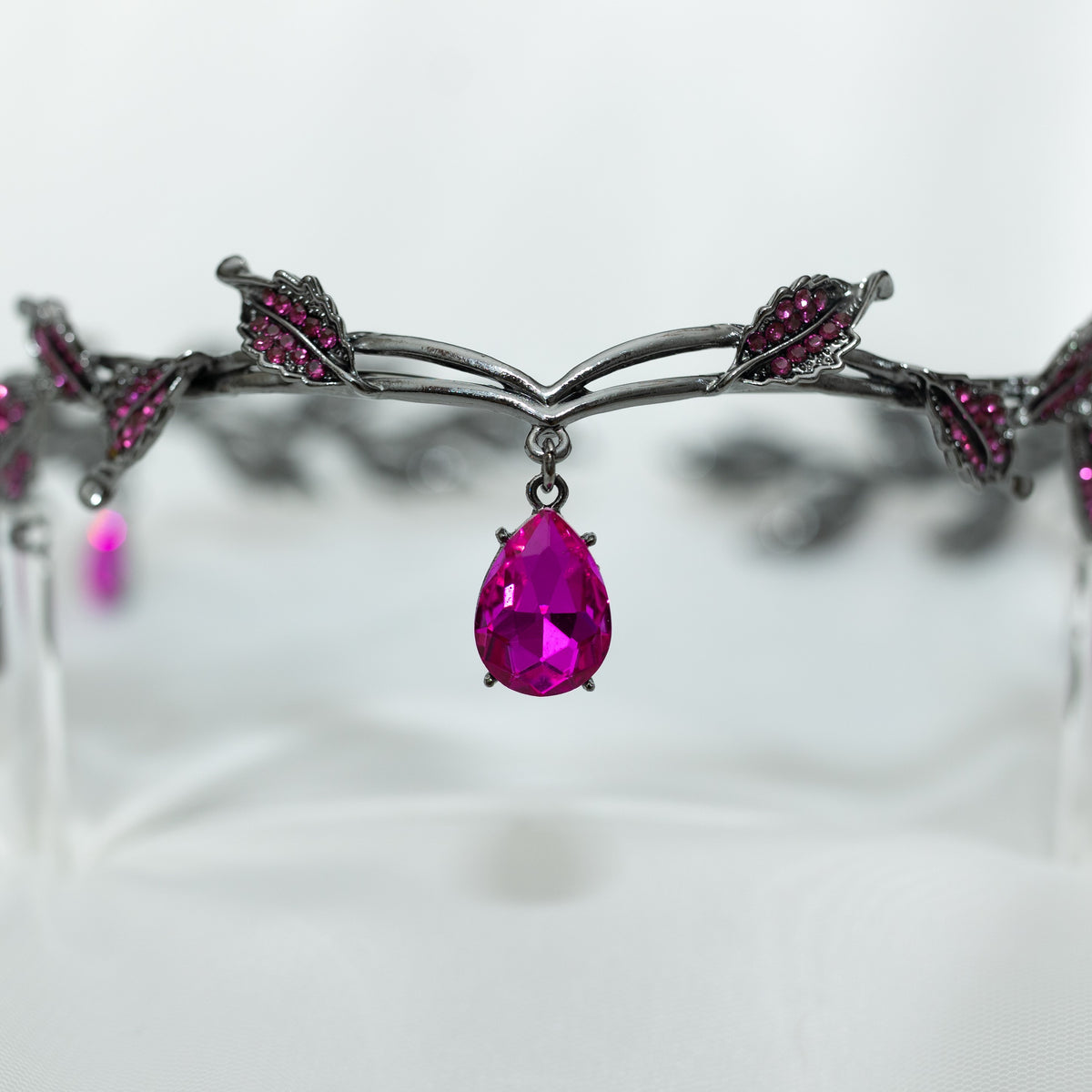 An elegant circlet featuring a hot pink crystal drop as the centerpiece, antique silver color metal with leaf-shaped embellishments and smaller pink crystals, set against a white background.
