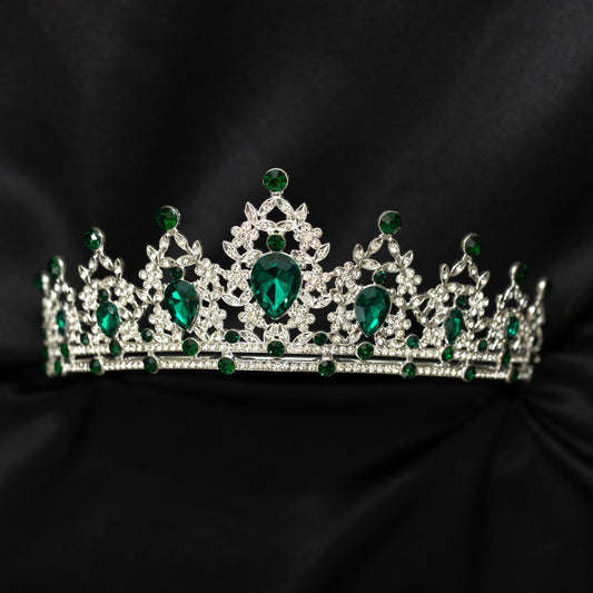 A sparkling tiara featuring green colored crystals set in a silver colored metal structure, displayed against a black background.
