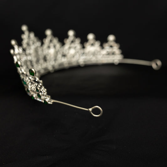 A sparkling tiara featuring green colored crystals set in a silver colored metal structure, displayed against a black background. End view 