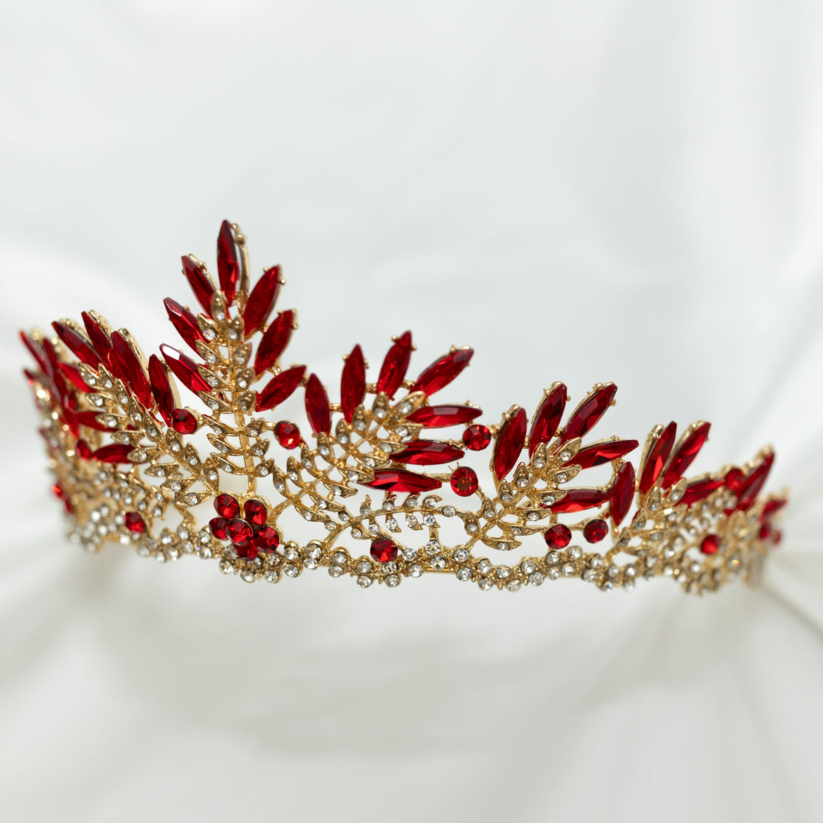 A golden tiara adorned with sharp spikes of red colored crystals against a white background. Front side view 