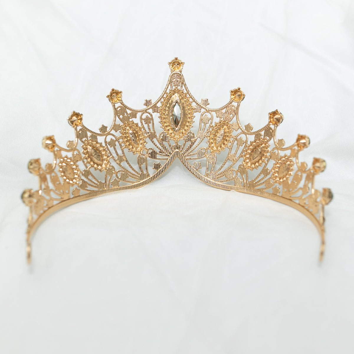 A golden tiara adorned with large green marquise shaped crystals and small clear round crystals, set against a white background. Rear view 