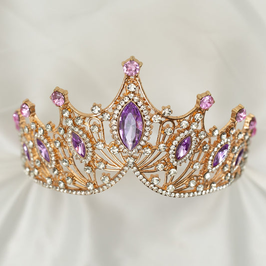 A Lavender and Gold tiara with marquise shaped crystals and clear round crystal detailing on a gold-colored metal structure, displayed against a white fabric background. Front view 