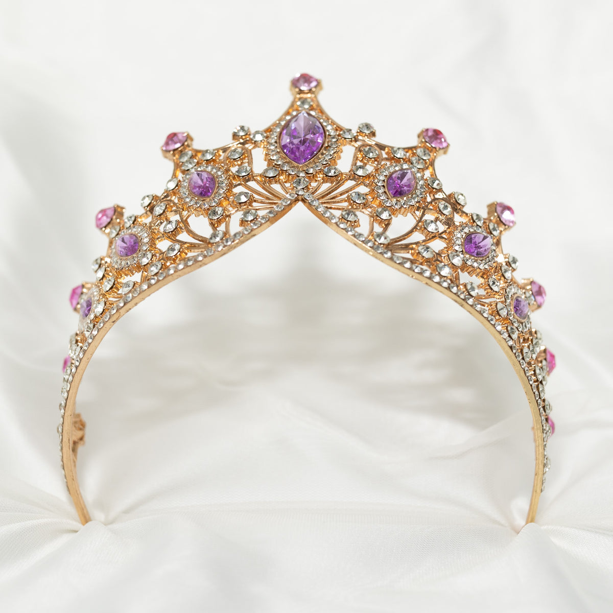 A Lavender and Gold tiara with marquise shaped crystals and clear round crystal detailing on a gold-colored metal structure, displayed against a white fabric background. Bottom view 