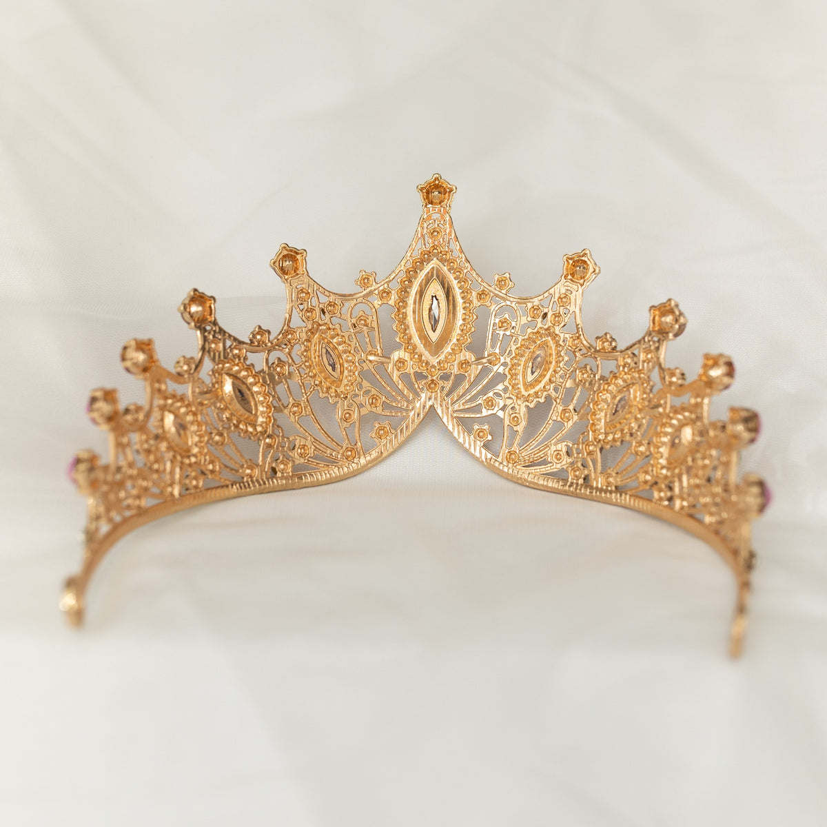 A Lavender and Gold tiara with marquise shaped crystals and clear round crystal detailing on a gold-colored metal structure, displayed against a white fabric background. Rear view 