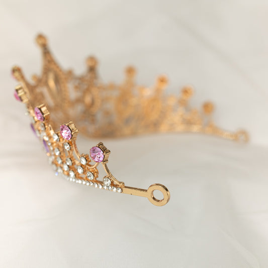 A Lavender and Gold tiara with marquise shaped crystals and clear round crystal detailing on a gold-colored metal structure, displayed against a white fabric background. End view 