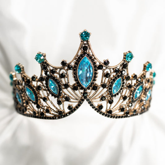 A light blue and antique gold tiara with large blue marquise shaped crystals and small black round crystal detailing, set against a white background.