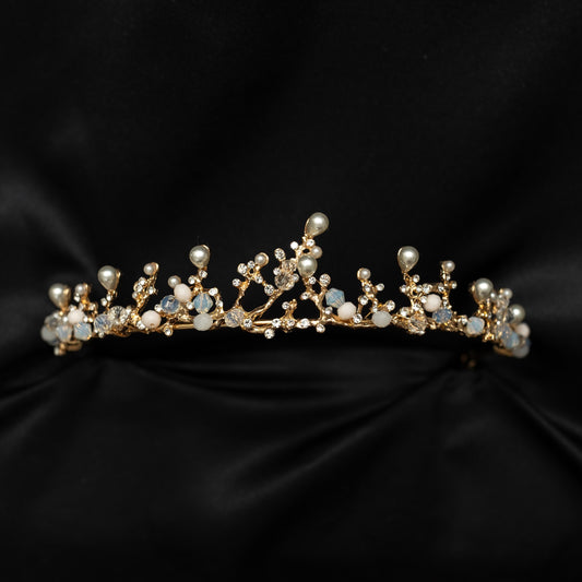 A delicate gold tiara adorned with white pearls and blue gemstones, displayed against a black background.