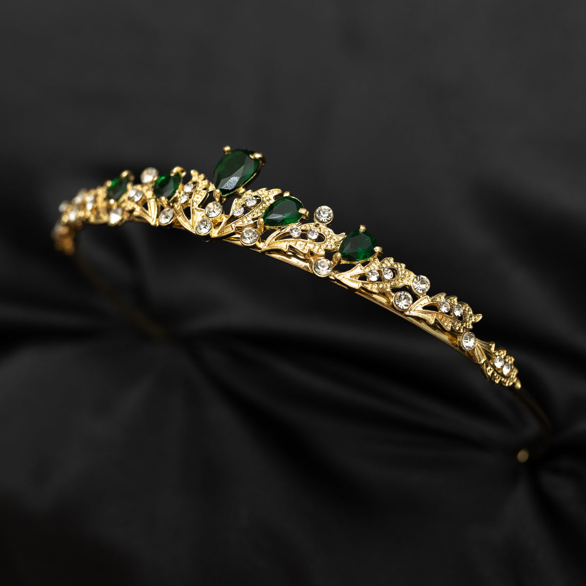 Gold tiara with green gemstones on a black fabric background