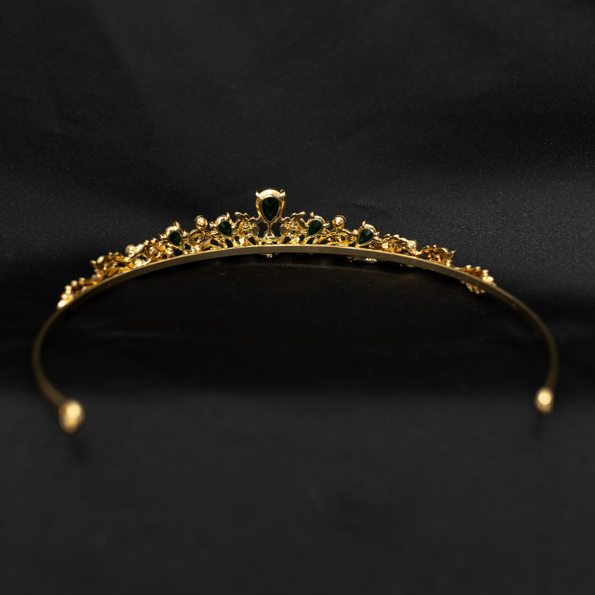 Gold tiara with green gemstones on a black background