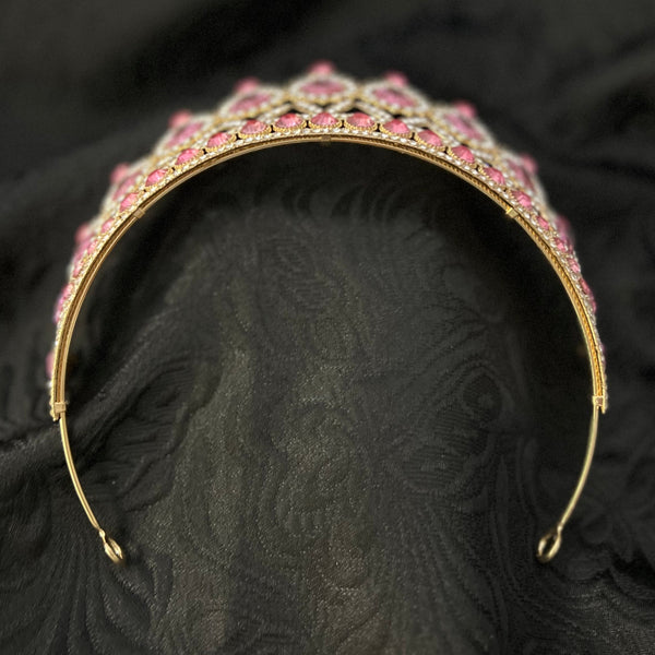 A gold-plated metal tiara headband embellished with pink rhinestones, displayed on a textured black fabric background.