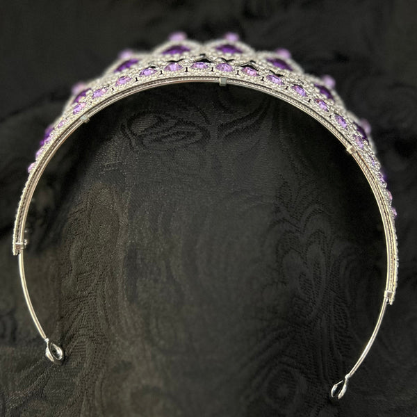 A silver-toned metal tiara headband embellished with small purple crystals, displayed on a textured black fabric background.