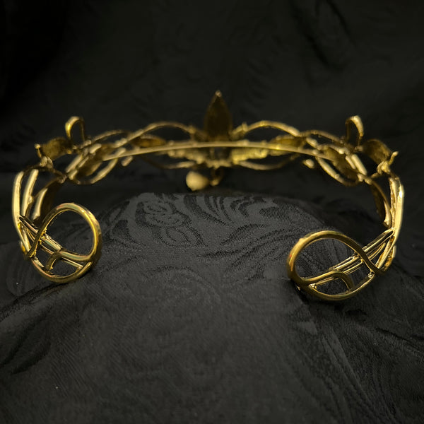 A close-up of a gold-toned metal handle with an ornate, leaf-like twisted design, mounted on a black damask fabric background.