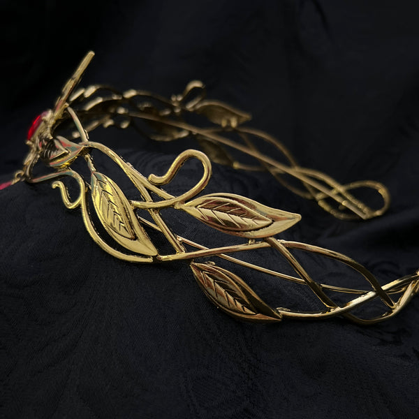 A gold-toned metal vine and leaf filigree accessory laid on a dark black fabric background.