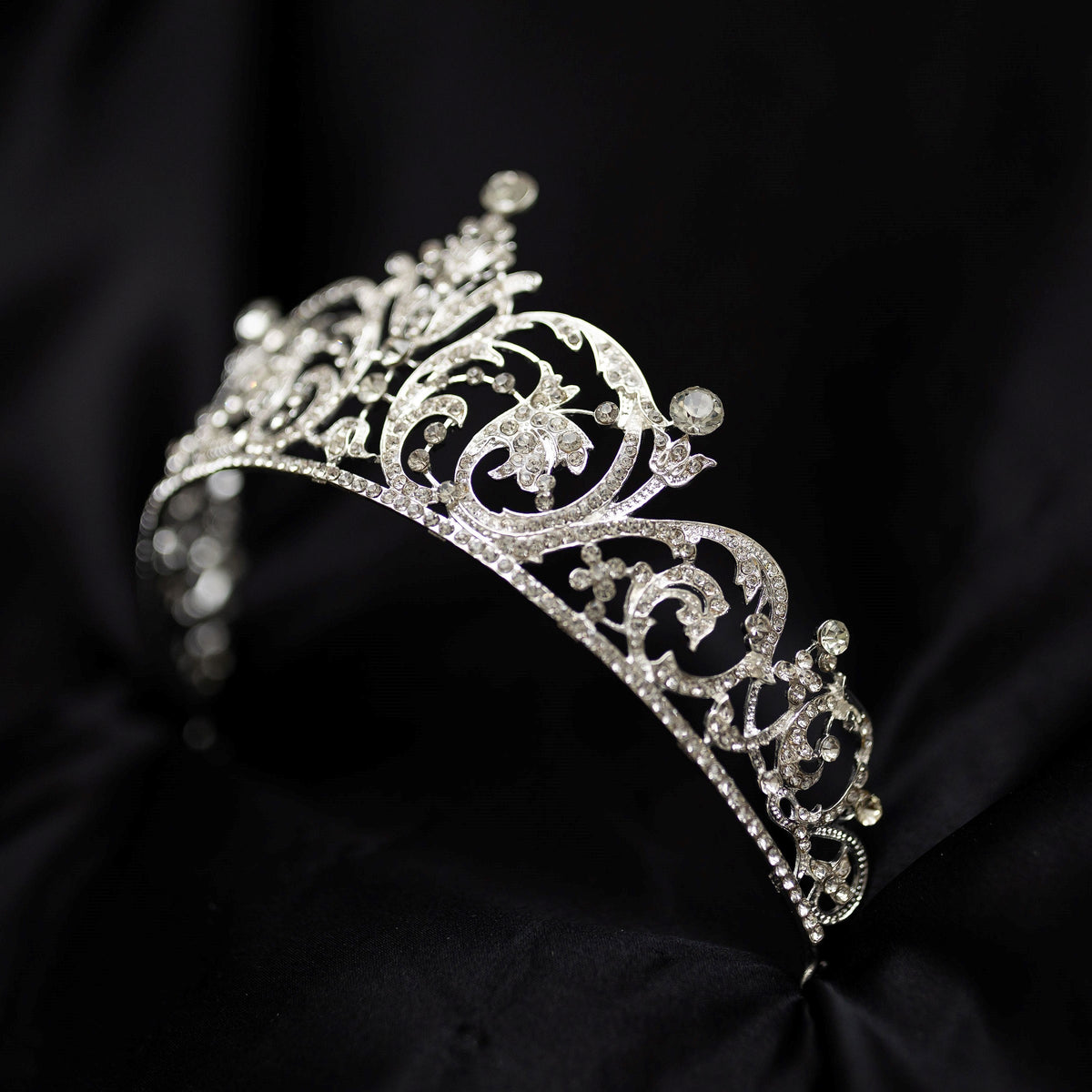 Elegant silver crystal tiara with intricate scrollwork design and sparkling rhinestones, photographed on a black background - Front Angle View 