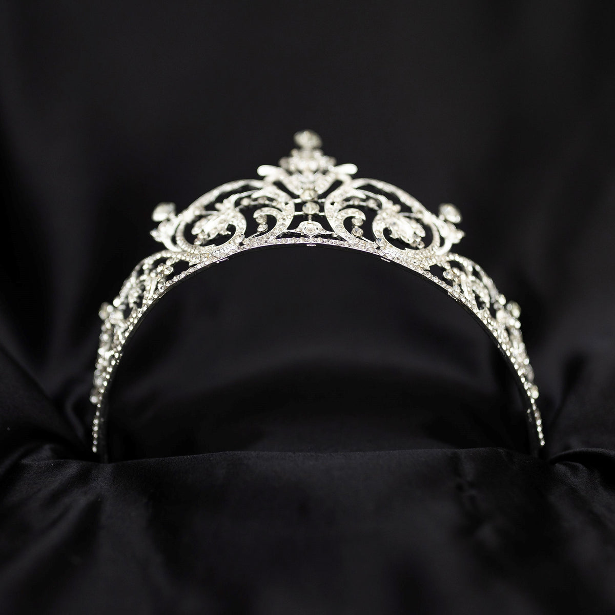 Elegant silver crystal tiara with intricate scrollwork design and sparkling rhinestones, photographed on a black background - Bottom View 