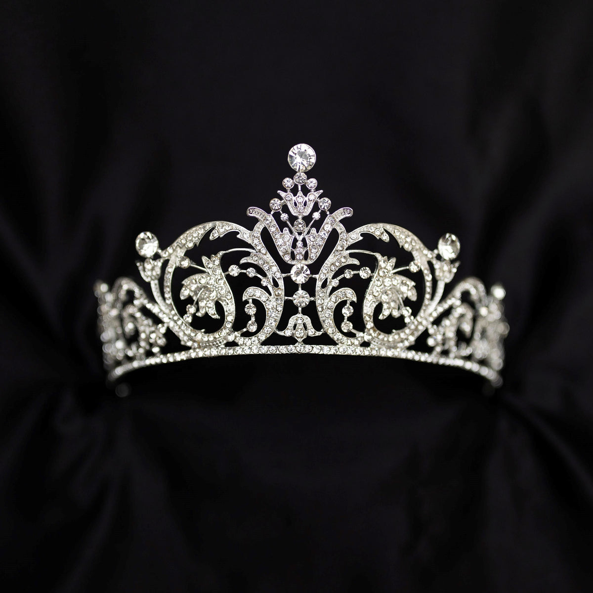 Elegant silver crystal tiara with intricate scrollwork design and sparkling rhinestones, photographed on a black background - Front View 