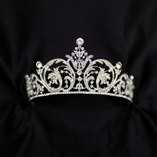 Elegant silver crystal tiara with intricate scrollwork design and sparkling rhinestones, photographed on a black background - Front View 