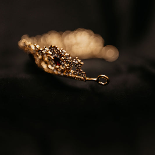 Benjamina's Tiara - A gold-colored metal tiara with clear crystal detailing and red gemstones set in the center, on a black background -  Looped End View 