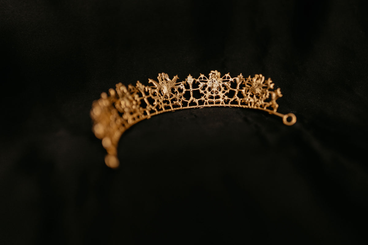 Benjamina's Tiara - A gold-colored metal tiara with clear crystal detailing and red gemstones set in the center, on a black background - Back View