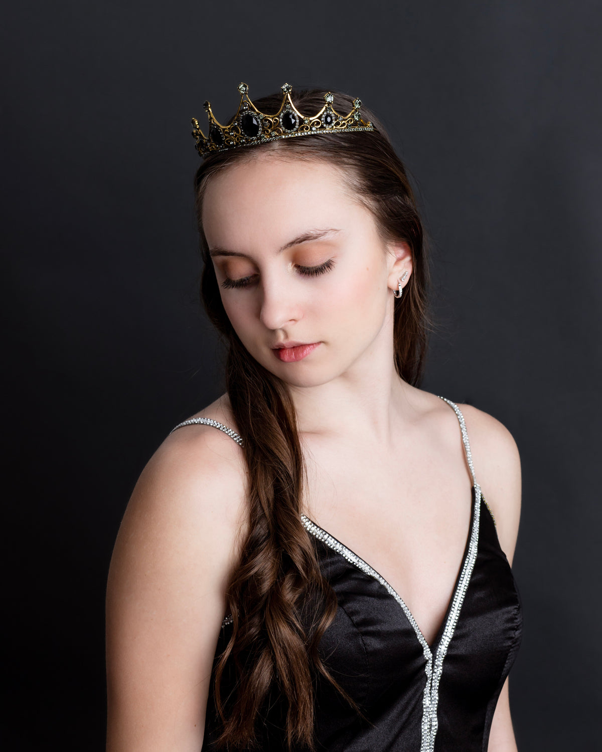 A baroque-style tiara with black colored crystals set in a yellow gold color setting, with loops on each end for securing to hair - Modeled