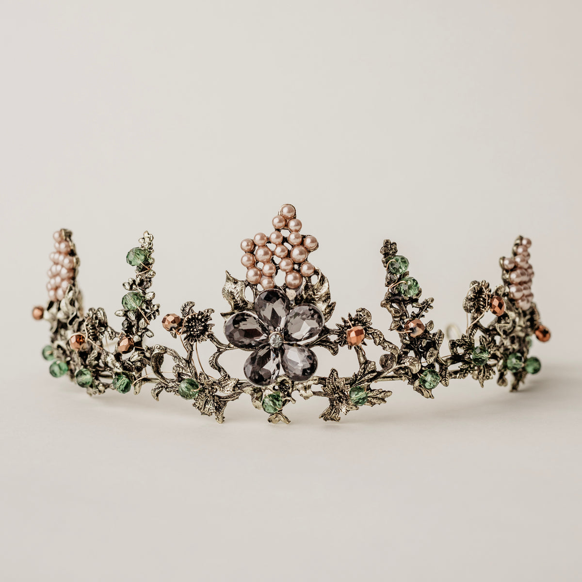 Antique gold-colored metal tiara with a large flower focal point, pearl details, green and copper colored beads, and loops on each end for securing to hair.