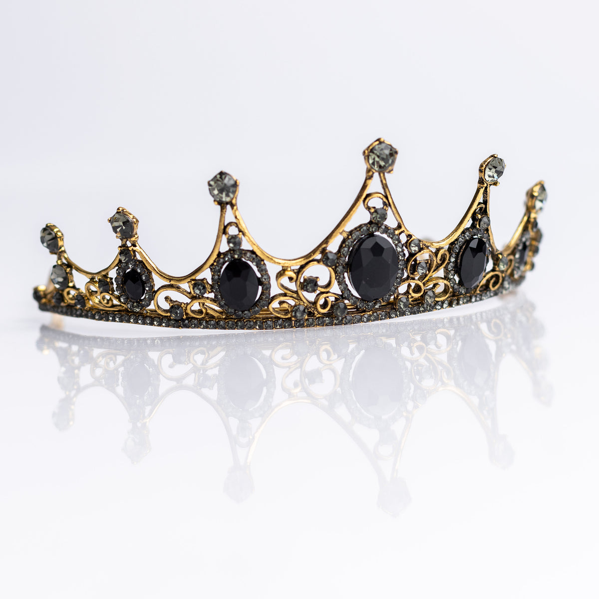 A baroque-style tiara with black colored crystals set in a yellow gold color setting, with loops on each end for securing to hair -  Front Angle View